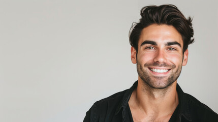Fototapeta premium A young man with dark hair and a broad smile exudes confidence and friendliness, set against a simple backdrop.