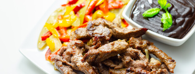 A plate of meat and vegetables with a sauce on the side