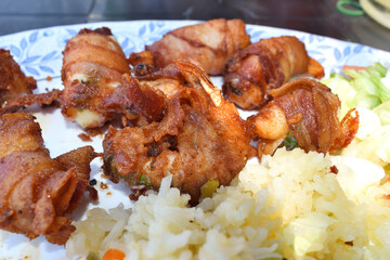 Close up of a dish called mummy shrimp, which are shrimp wrapped with bacon, accompanied by rice and salad, in a restaurant