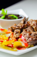 A plate of meat and vegetables with a sauce on the side