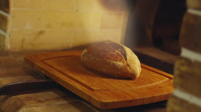 Close up of freshly baked aromatic loaf of wholemeal rye bread in a traditional stone oven on fire, aromatic smoke rises above the bread