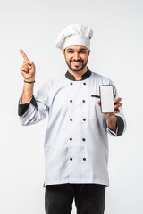 Indian Asian young chef in uniform presenting empty smartphone and white plate on white background