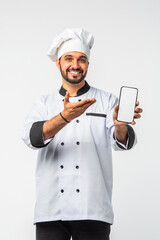 Indian Asian young chef in uniform presenting empty smartphone and white plate on white background