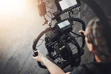 Fototapeta premium Videographer, camera and man filming in studio for photography, production and media. Behind the scenes, backstage and person with stabilizing equipment on set shooting videos, documentary or film