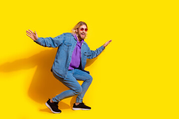 Full body photo of attractive young man sunglass surfing balance dressed stylish denim clothes isolated on yellow color background