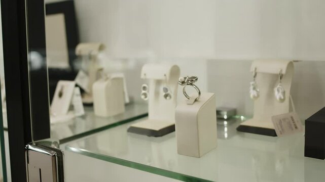 No people shot of exlusive dainty precious metal earrings and ring displayed in crystal-clear showcase in luxury pemium jewellery showroom