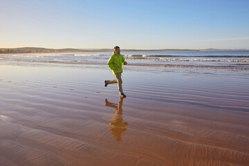 A young man in a green jacket enjoys a coastal run along Essaouira's ocean