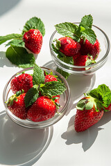 Fresh strawberries with mint leaves in glass bowls, bathed in natural sunlight, showcasing a healthy summer snack.