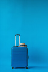 A blue suitcase stands against a vibrant blue background, with a straw hat and sunglasses resting on top, symbolizing travel and adventure.