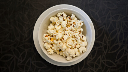 Bowl of Freshly Popped Popcorn on White Plate with Black Patterned Background