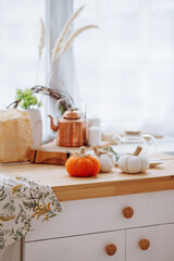 Bright kitchen with wooden kitchen utensils and three decorative pumpkins. Stylish decor concept for home, Halloween or autumn harvest.