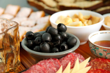 Olives, sausage, and cheese arranged on a serving dish with honey on a rustic table. Mediterranean appetizer spread featuring olives on a serving dish