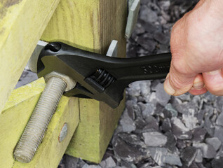 Closeup of a man’s hand using an adjustable wrench to tighten a nut on a large bolt going through...