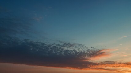Obraz premium A vibrant sunset sky with a striking gradient of blue and orange hues and scattered clouds, creating a serene and picturesque evening landscape