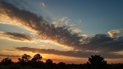 Obraz premium A serene sunset with dramatic cloud formations and a glowing orange and yellow sky, creating a peaceful and scenic end to an evening in nature