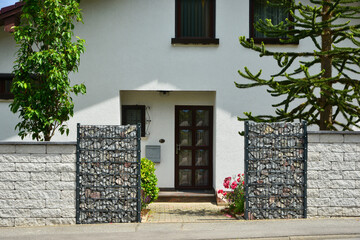 Moderner Sichtschutzzaun aus mit Naturstein gefüllten Gabionen und Betonstein-Mauer um ein neu bebautes Grundstück © Hermann