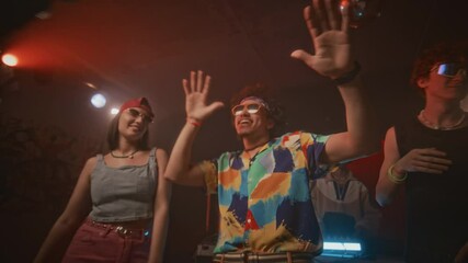 Lowkey shot of charismatic and energetic hipster guy in aviator sunglasses, fancy shirt and with puffy hair dancing in centre of dance floor among trendy ravers to edm in nightclub with flashes