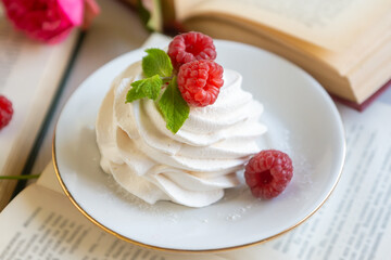 Sweet raspberries in a porcelain cup on a table with books.