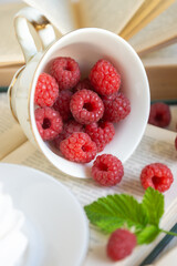 Sweet raspberries in a porcelain cup on a table with books.