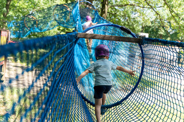 Children exploring rope course in adventure park with safety helmets. Concept of outdoor adventure,...