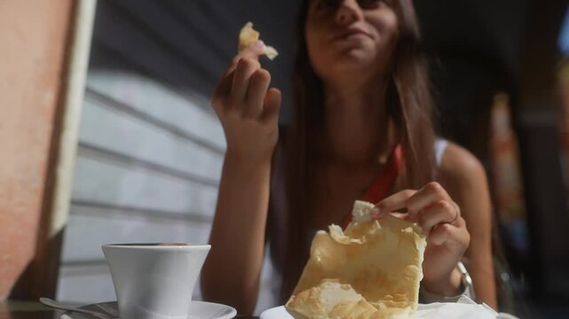 A woman is happily snacking and enjoying her coffee outside, under the sunlight