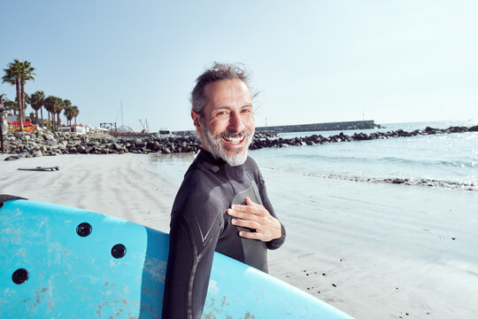 portrait happy mature surfer man on the beach holding a surfboard