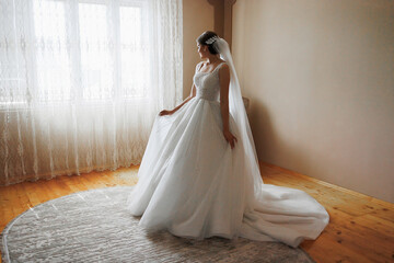 Fototapeta premium A bride is standing in front of a window in a room. She is wearing a white dress and a veil