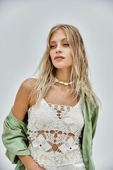 A blonde woman in a white crochet top poses against a grey backdrop.