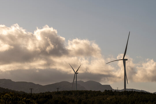 This breathtaking image captures wind turbines against a backdrop of mountains and a cloudy sky at sunset, symbolizing the merge of advanced technology and picturesque nature.