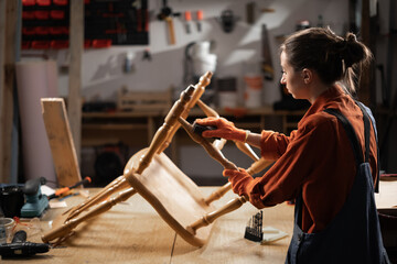 woman restoring furniture sanding old wooden chair in workshop with dark light