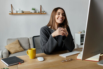 A young woman smiles brightly as she works on her computer in her home office.