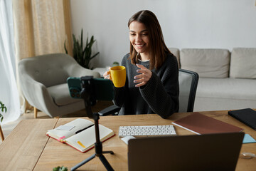 A young woman smiles as she films a video from her home office, enjoying a warm beverage.