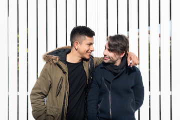 young male gay stylish couple standing together hugging, smiling and looking at each other outdoors...