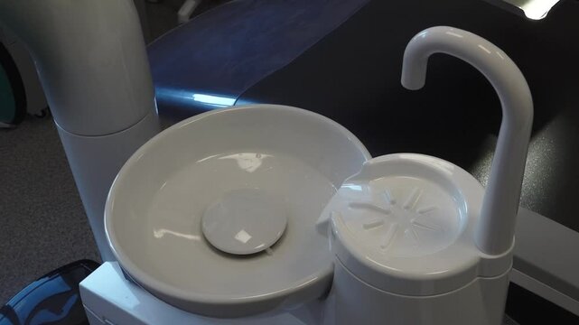 Close-up of a white dental sink and spittoon in a modern dental clinic, showing clean and sterile equipment.