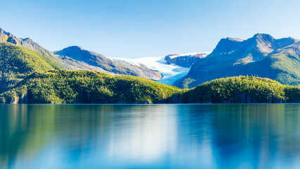 Scenic view of Svartisen Glacier atop lush green hills by the fjord along the helgelandkysten National Tourist Road. Longexposure shot. Beauty of North Norway.