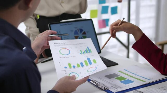 Business professionals discussing sales charts, graphs, and marketing reports in a collaborative meeting. Engaged teamwork and data analysis in a modern office setting