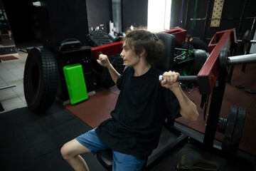 man in a black t-shirt performs a shoulder press exercise at a gym, lifting weights with his arms...