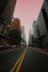 Low-angle view of a city street with skyscrapers and a pink sky at dusk in New York City