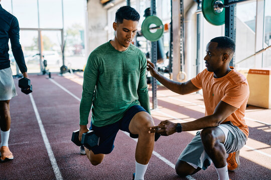 Instructor giving encouragement to a fit young man working out with dumbbells during a strength training session in a gym