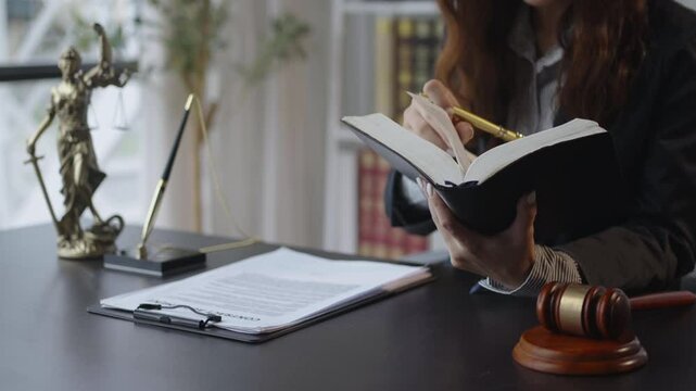 Judge meticulously reviews legal documents and annotates a law book at a desk with a gavel and justice statue