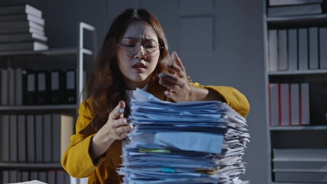 Stressed office worker sorting through a towering stack of paperwork in cluttered workspace, displaying frustration and fatigue