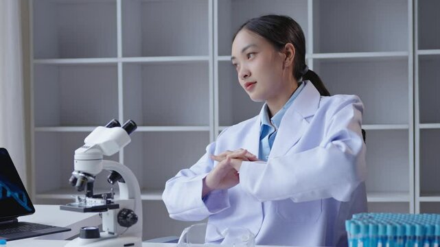 Female scientist taking a quick stretch break in a laboratory, surrounded by scientific equipment and test tubes. She is seated at a desk with a microscope and laptop, balancing work and relaxation