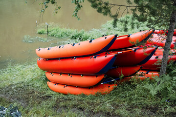 A group of orange kayaks is neatly stacked by a serene lake in a forested area, perfect for outdoor adventure and relaxation surrounded by the beauty of nature