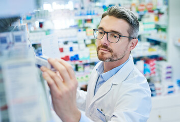Mature man, pharmacist and checking inventory with box for medical supplies, stock or medication at pharmacy. Male person or healthcare employee reading pharmaceuticals or drugs at dispensary store