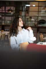 Young woman touching her hair and looking away while sitting at a restaurant table