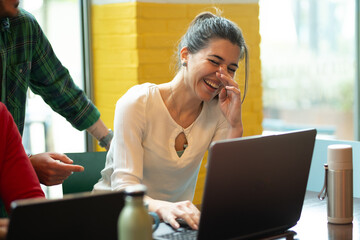 Young woman laughing while working on laptop at cafe with coworkers