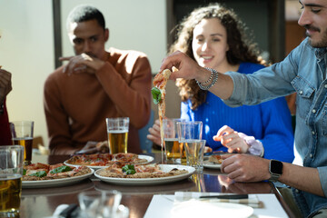 Man taking slice of pizza from plate with group of friends