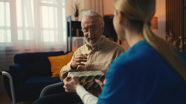 Senior man receiving present box from young woman volunteer, Christmas greeting