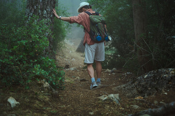 Hiker in forest taking a break, leaning on tree during a foggy day in nature