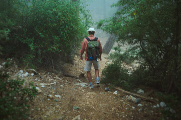 Obraz premium Man hiking on a foggy forest trail with a backpack in wilderness